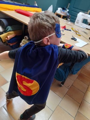 un enfant avec la cape et le masque de super héros qu'il a fabriqué