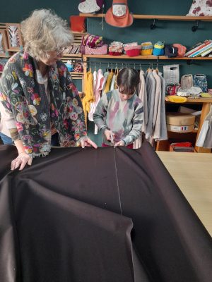 une jeune fille coupe du tissus aux côtés de sa grand mère